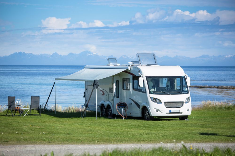 White Camper Van Parked on a Grassy Lakeshore With an Awning — Dempsters Caravan & RV in Gin Gin, QLD