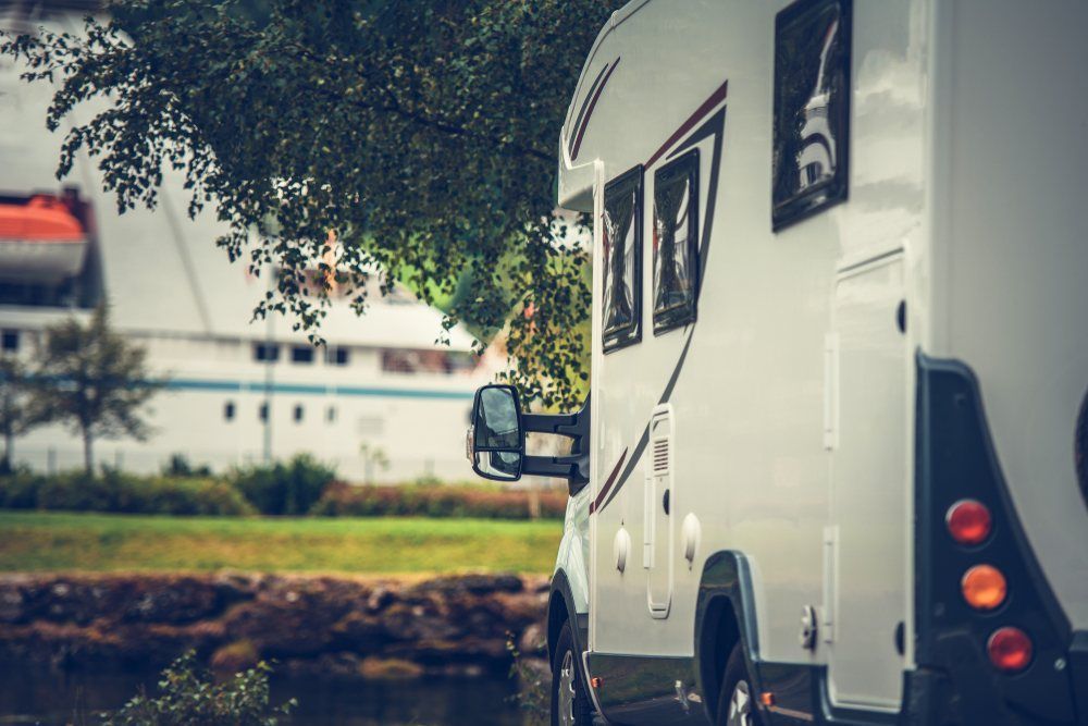 A White Rv is Parked Under a Tree Next to a Body of Water — Dempsters Caravan & RV in Bundaberg, QLD