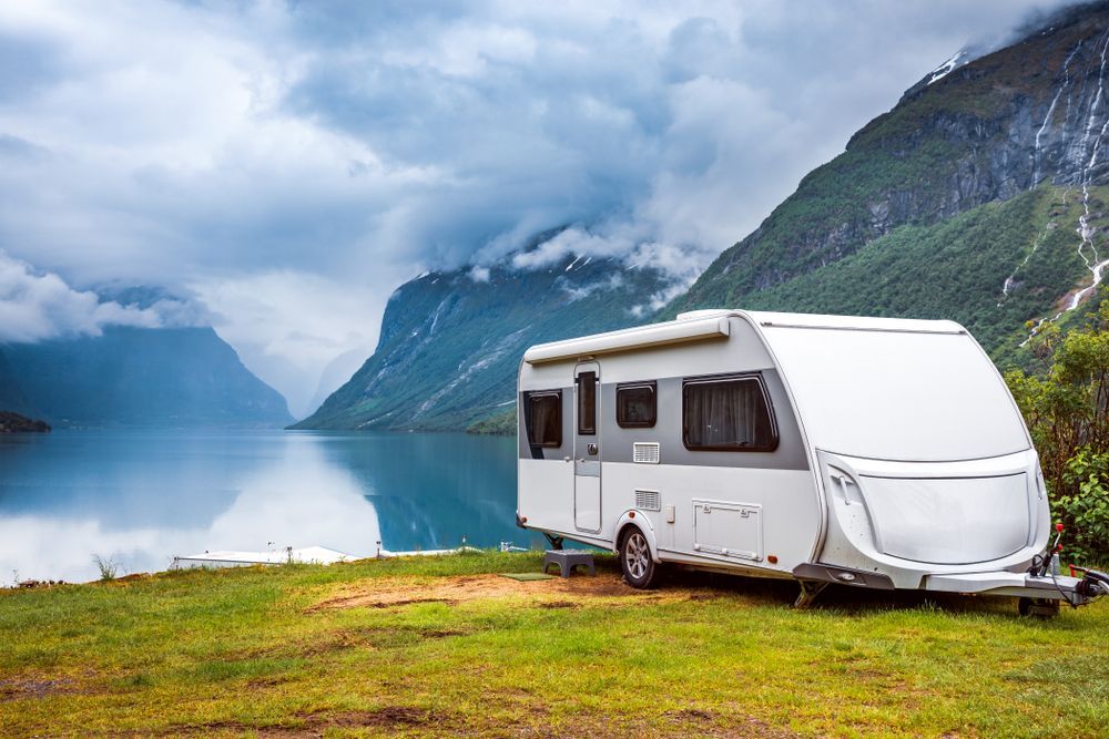 White Camper Van Parked by a Blue Fjord With Mountains — Dempsters Caravan & RV in Gin Gin, QLD