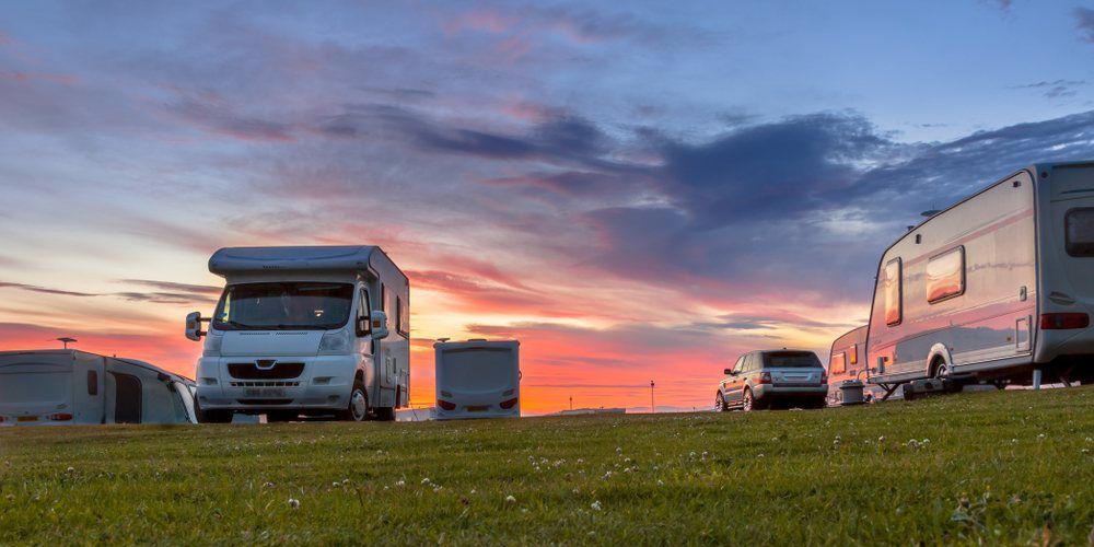 A Group of Rvs Are Parked in a Grassy Field at Sunset — Dempsters Caravan & RV in Bundaberg, QLD