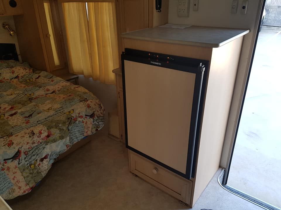 A Small Refrigerator is Sitting in a Bedroom Next to a Bed — Dempsters Caravan & RV in Thabeban, QLD