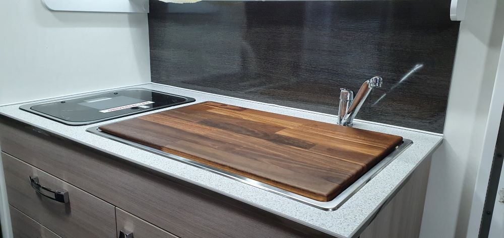 A Kitchen Sink With a Wooden Cutting Board on Top of It — Dempsters Caravan & RV in Thabeban, QLD