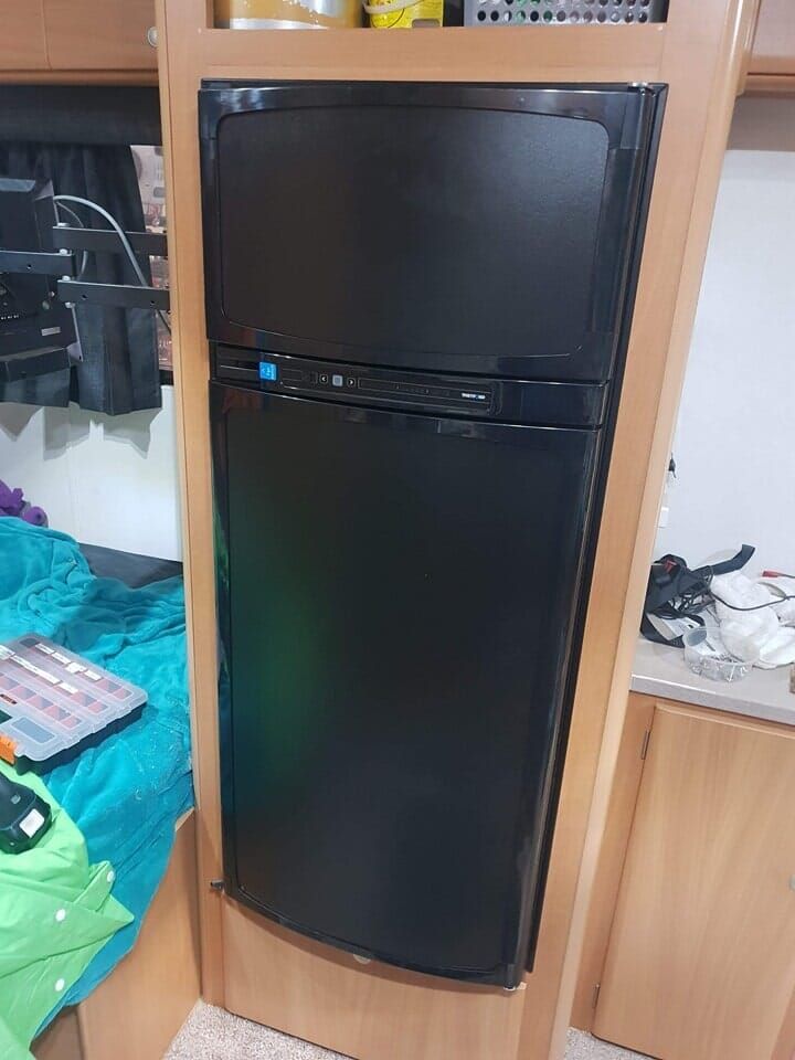 A Black Fridge is Sitting in a Wooden Nook in a Caravan — Dempsters Caravan & RV in Hervey Bay, QLD