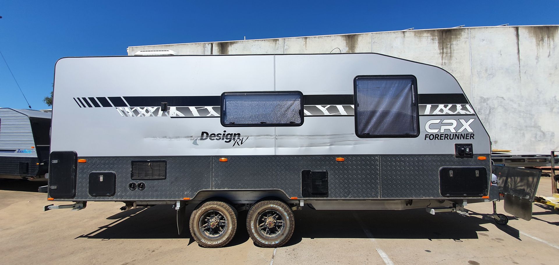 A White Caravan is Parked in a Garage With a Tire on the Ground — Dempsters Caravan & RV in Thabeban, QLD