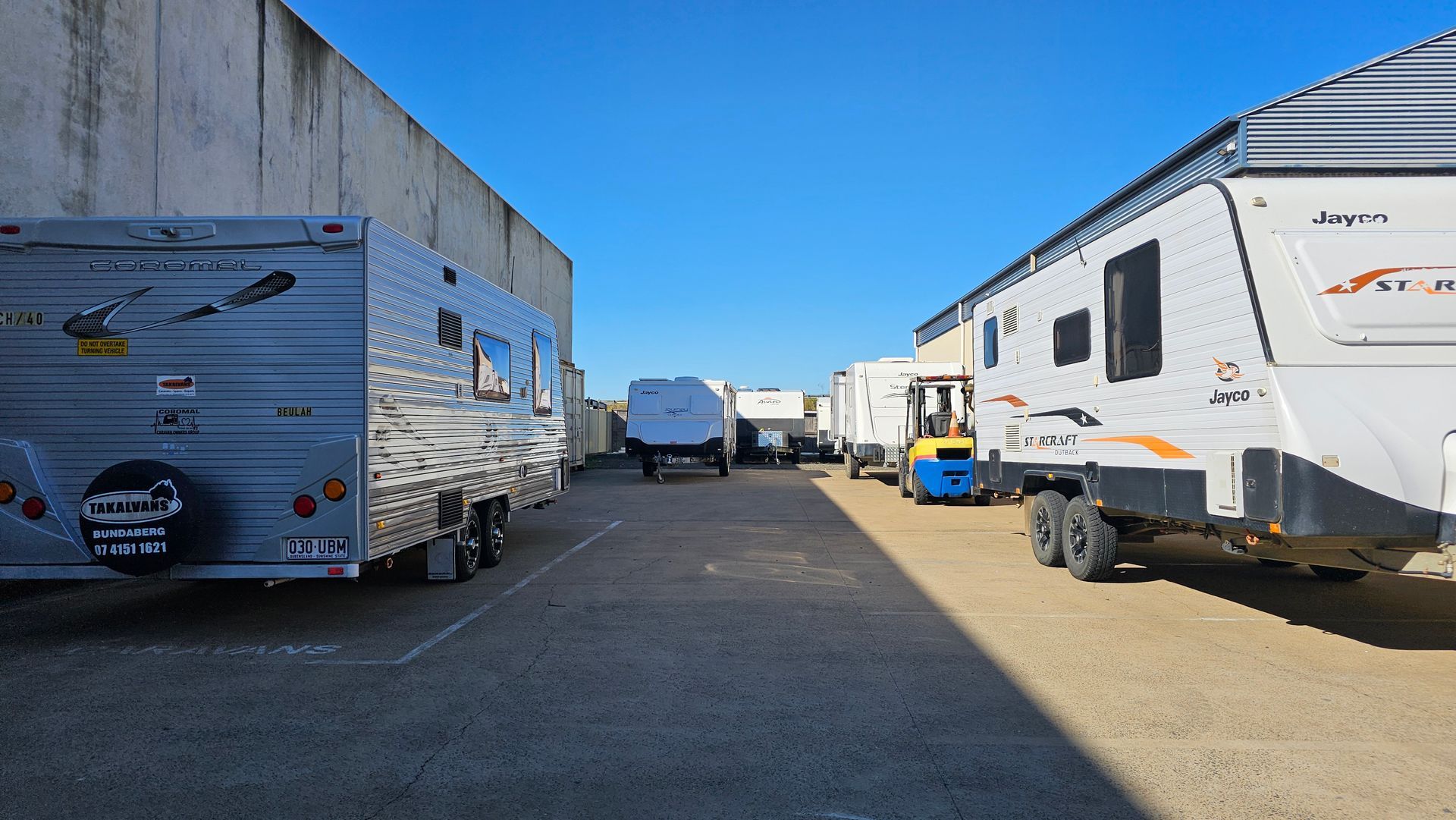 Row of Parked Rv Trailers in a Wide Gravel Lot Under a Clear Blue Sky — Dempsters Caravan & RV in Childers, QLD