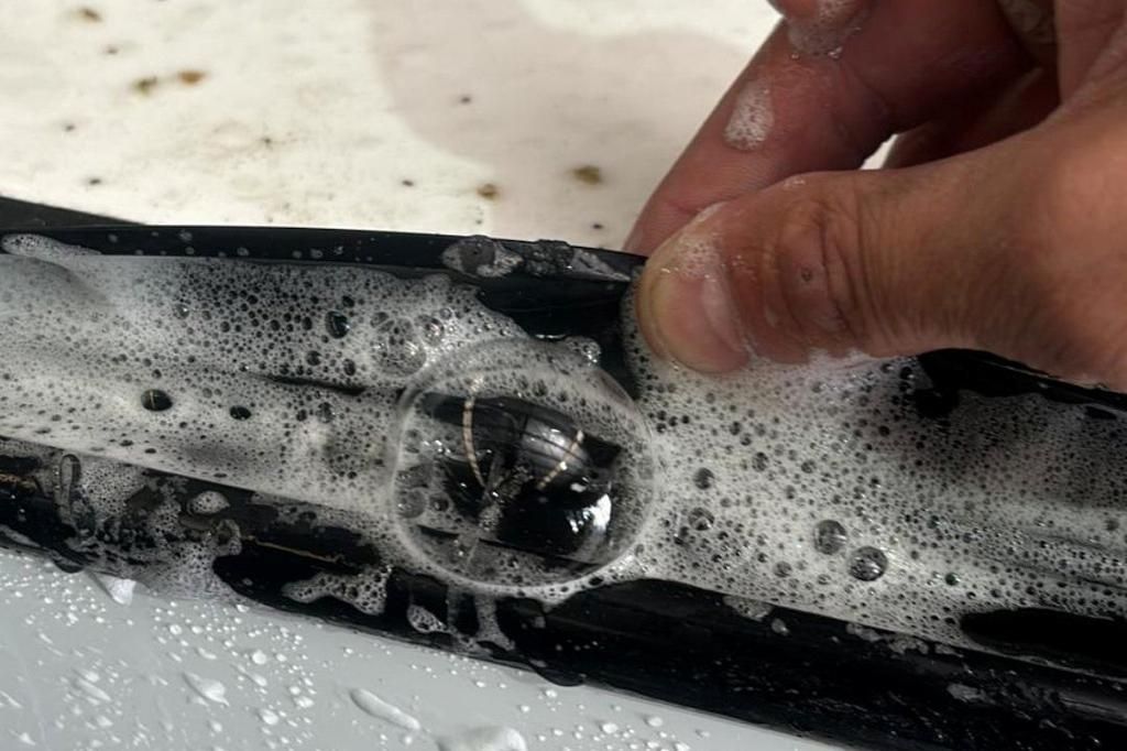 Hand holding a soapy black object with a clear circular part being cleaned under running water