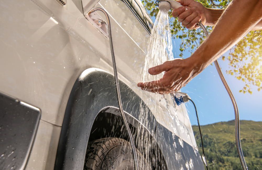 Hands Washing a White SUV With Water Spraying Over the Wheel Arch Outdoors — Dempsters Caravan & RV in Gin Gin, QLD