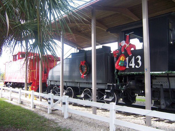Train engine and caboose painted in red and black, under a covered shelter. Santa decorations are visible on the train.