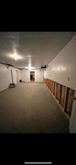 An unfinished, narrow room with a gray concrete floor, white ceiling, and exposed wall studs along the right side.