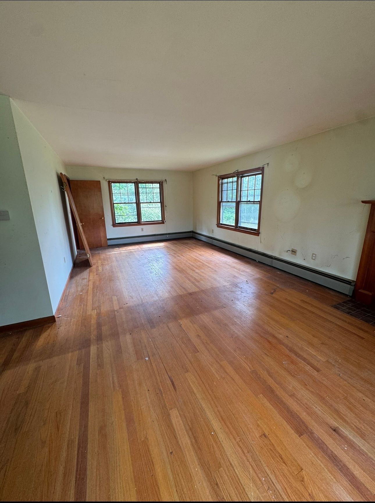 An attic interior with exposed wooden rafters, a plywood floor, and a window allowing light into the unfinished space.