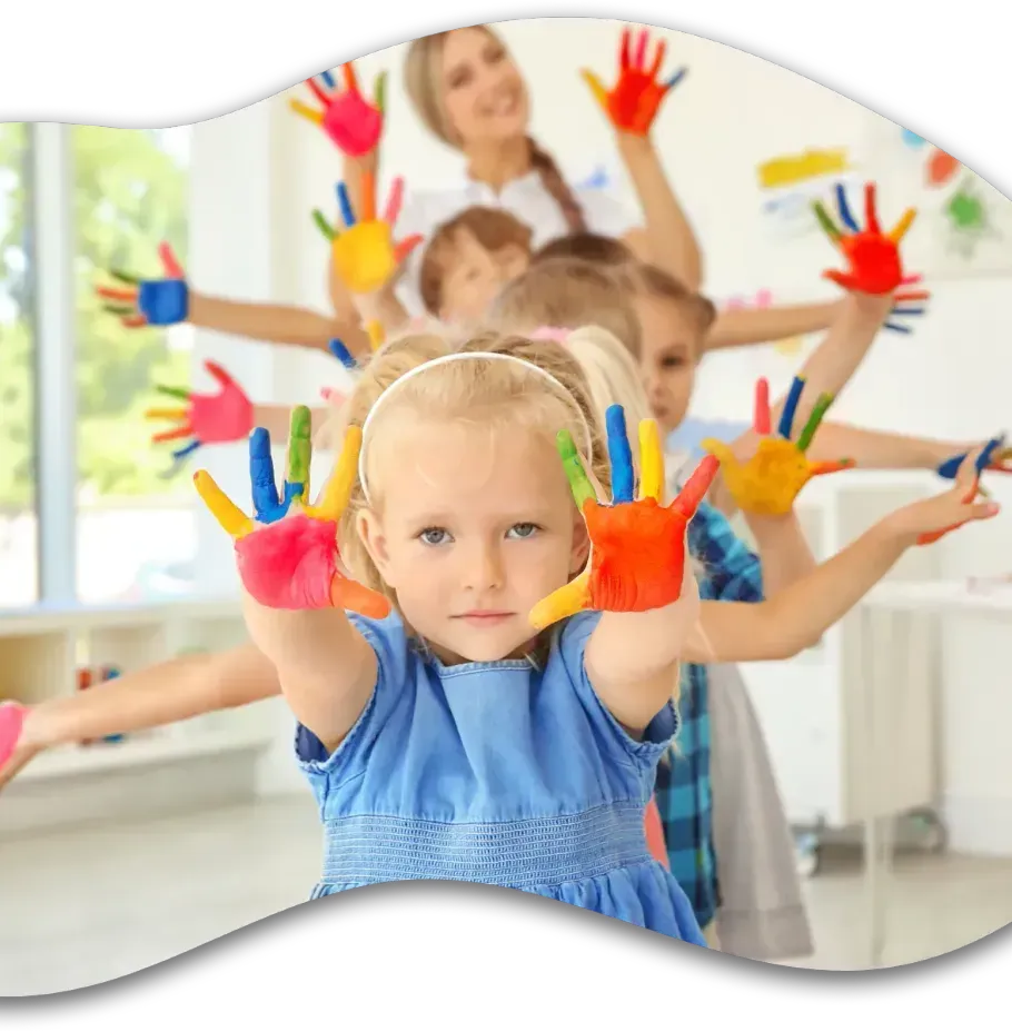 A teacher and children in a classroom hold up their hands covered in colorful, bright paint.