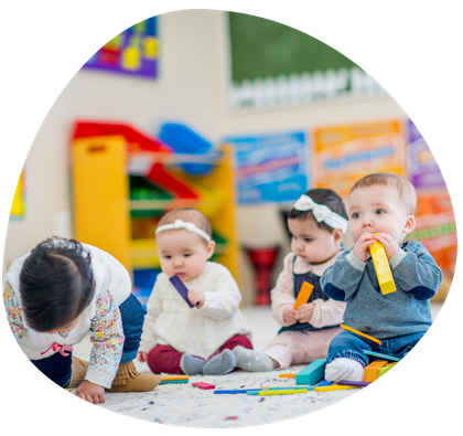 Four toddlers play with colorful wooden blocks on a rug in a brightly colored classroom setting.