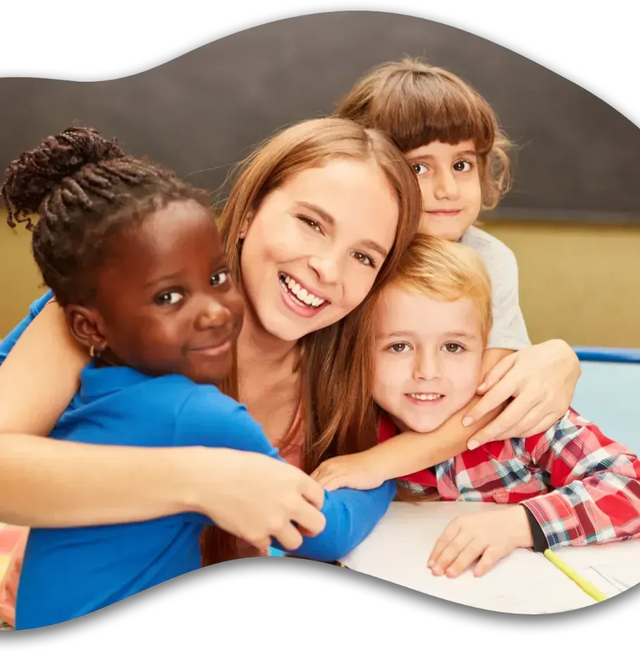 A smiling teacher embraces three students in a classroom setting.