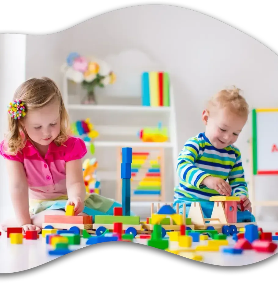 Two children sit on the floor playing with colorful wooden building blocks and a toy train in a bright, sunny room.