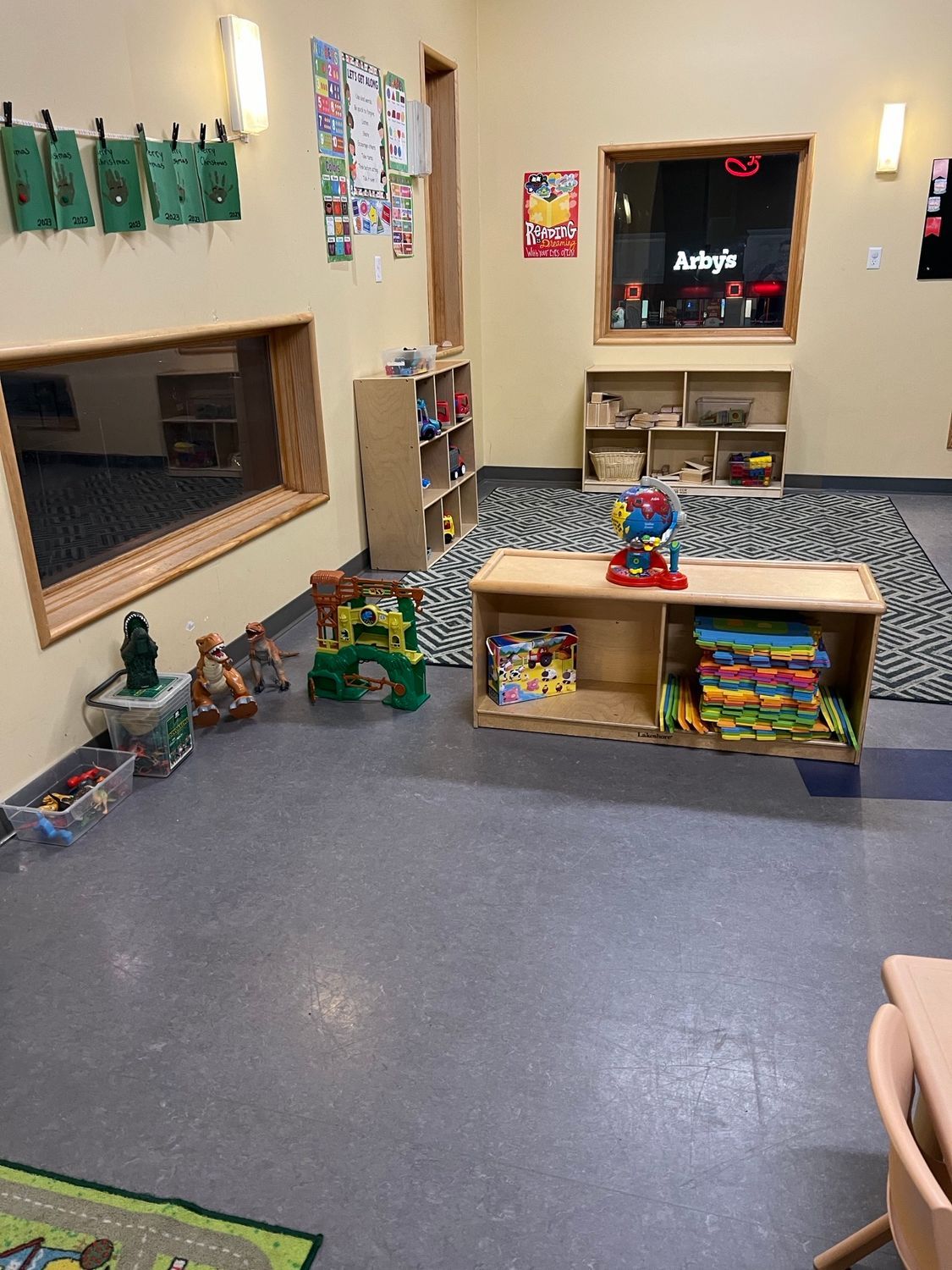 A brightly lit children's playroom with cubby shelves, toys, a patterned rug, and wall decorations.