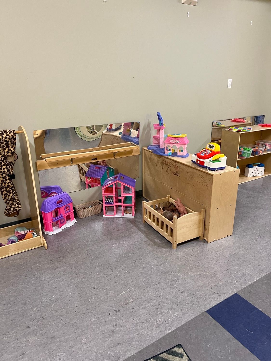 A playroom area with a wooden shelf holding a toy car and building, plus a small crib and dollhouse on the floor.
