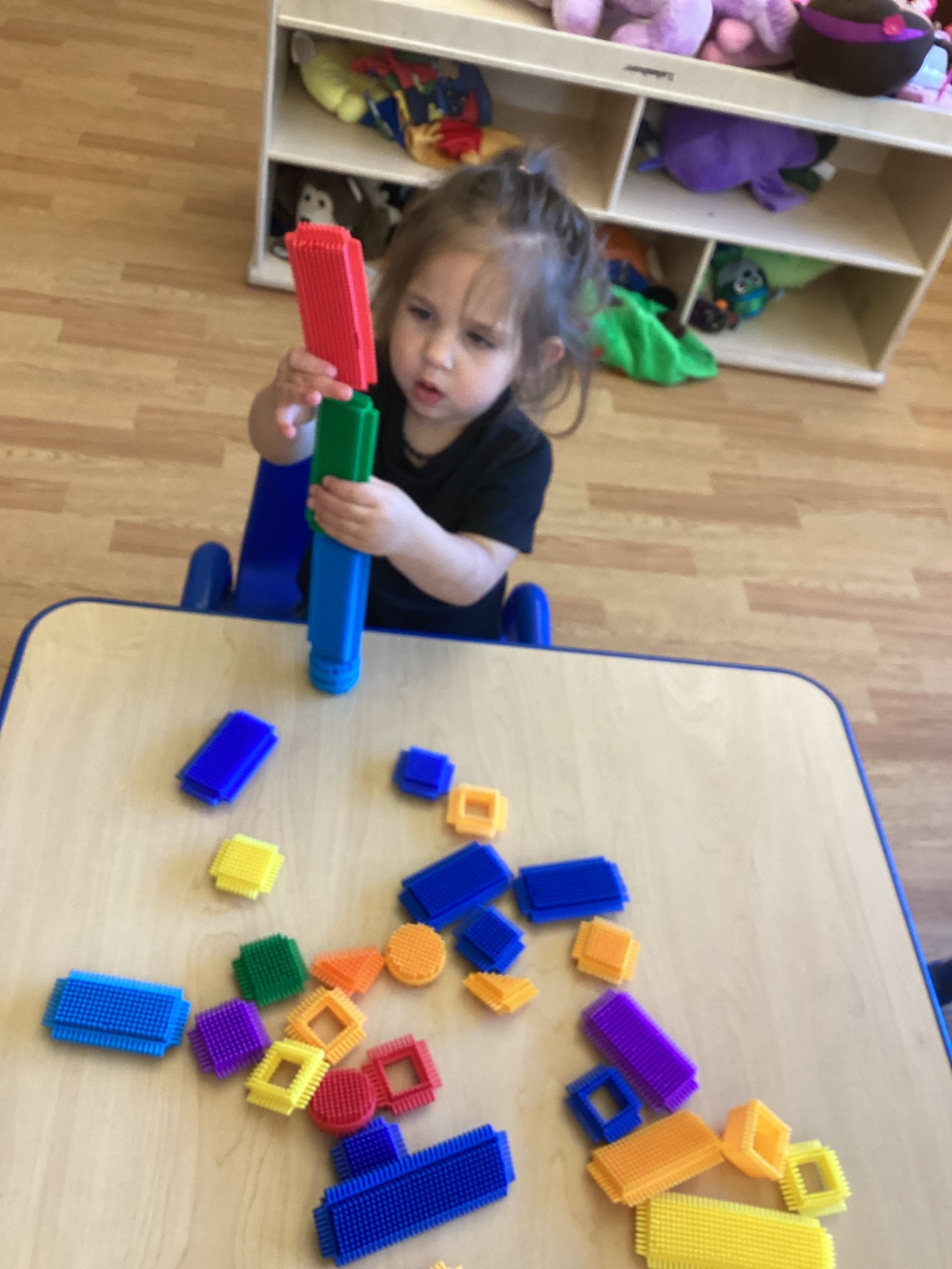 A person seated at a table stacking colorful interlocking plastic building blocks.