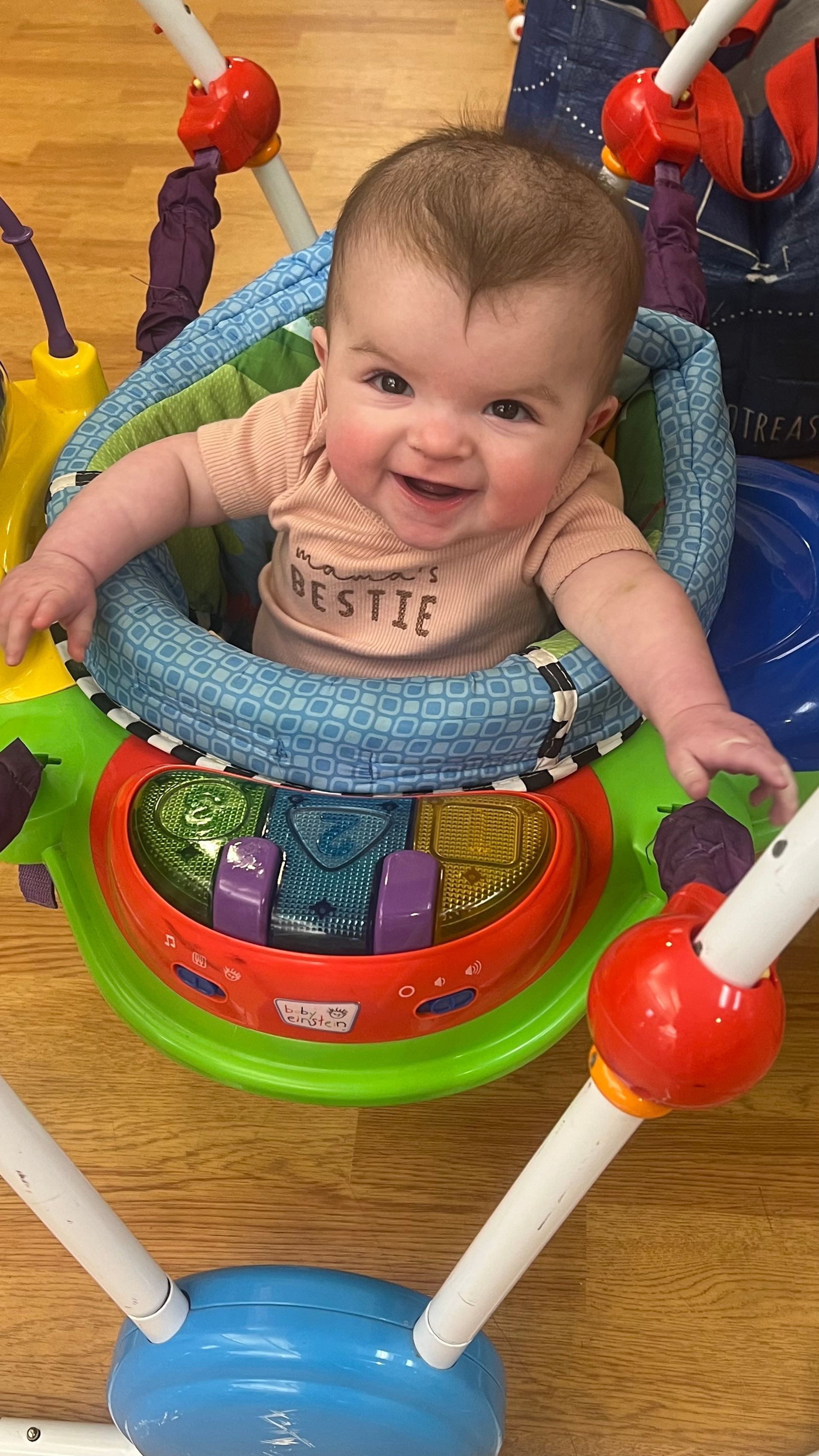 A smiling baby in a brightly colored activity jumper.