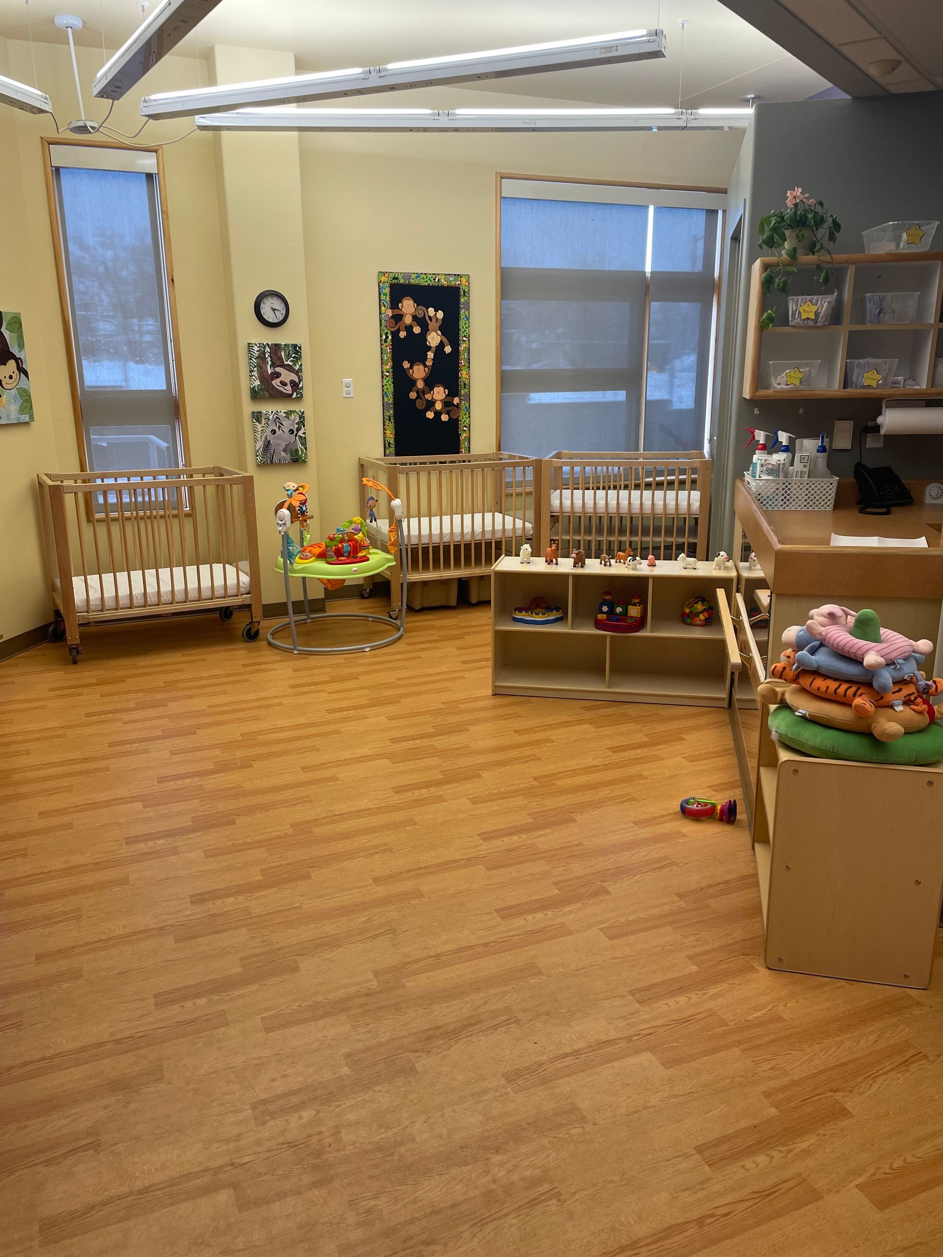 A room with wooden cribs, a low storage shelf, changing table, and wood-patterned flooring.
