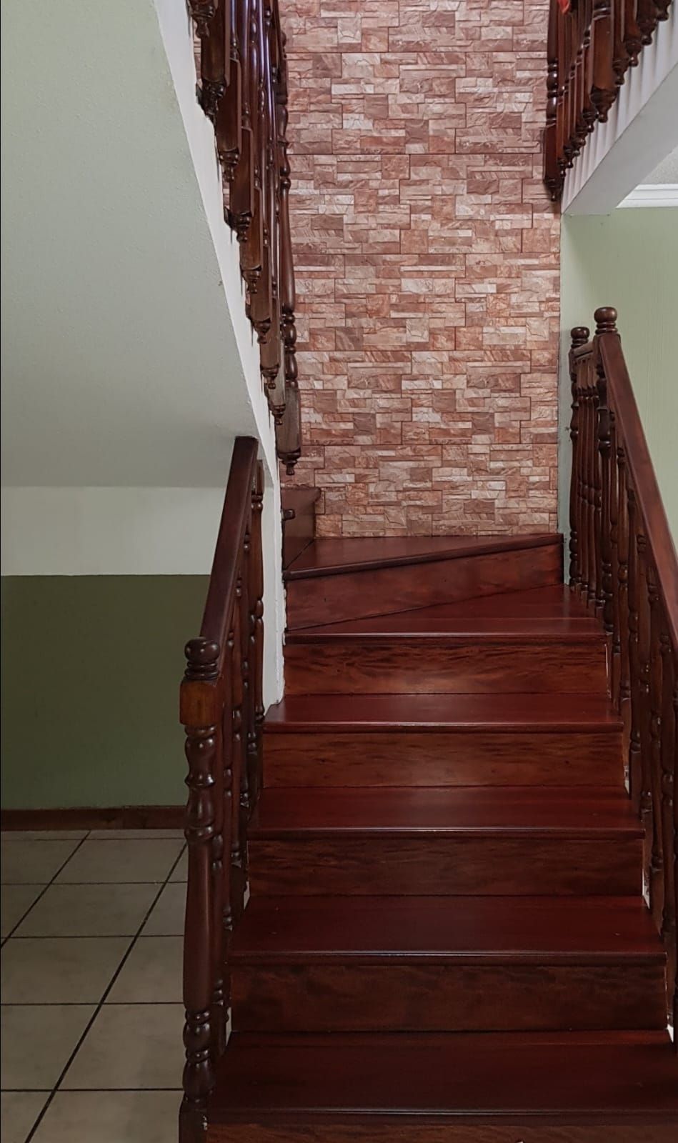 Escalera interior de madera con barandillas oscuras junto a una pared con diseño de ladrillos.