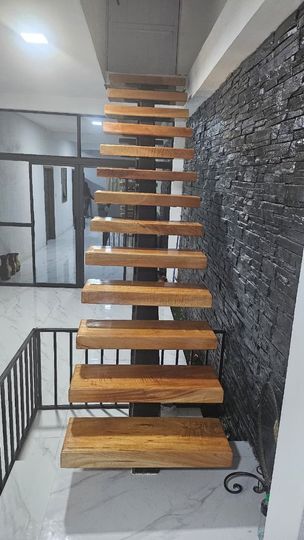Escalera flotante de madera con barandilla de metal negro en un pasillo interior moderno.