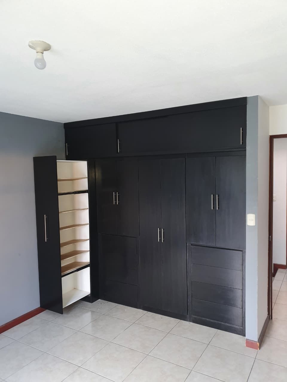 Habitación pequeña con armario y estantería negros, paredes grises y suelo de baldosas.