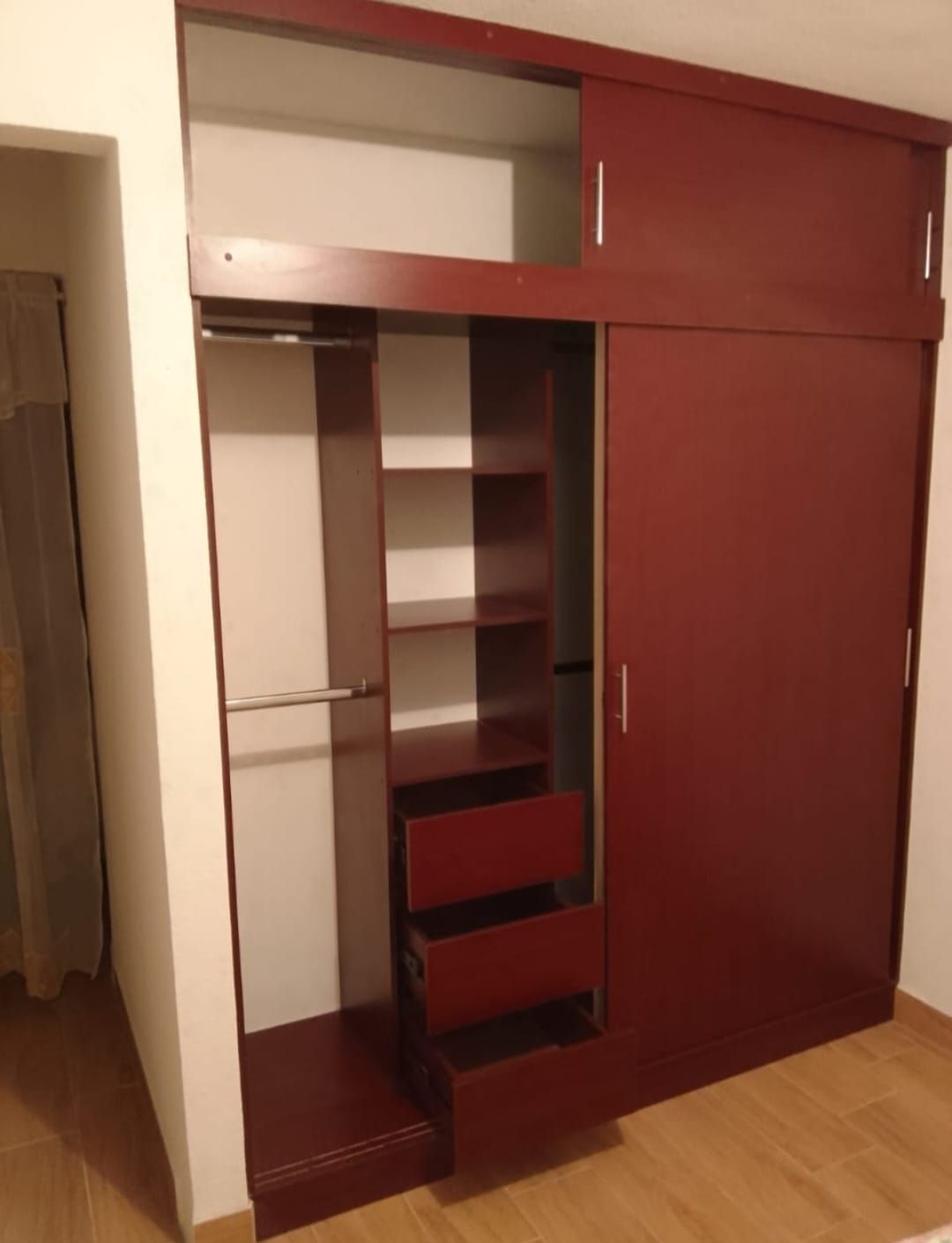 Armario empotrado color granate con estantes abiertos, cajones y una puerta corredera en una habitación.