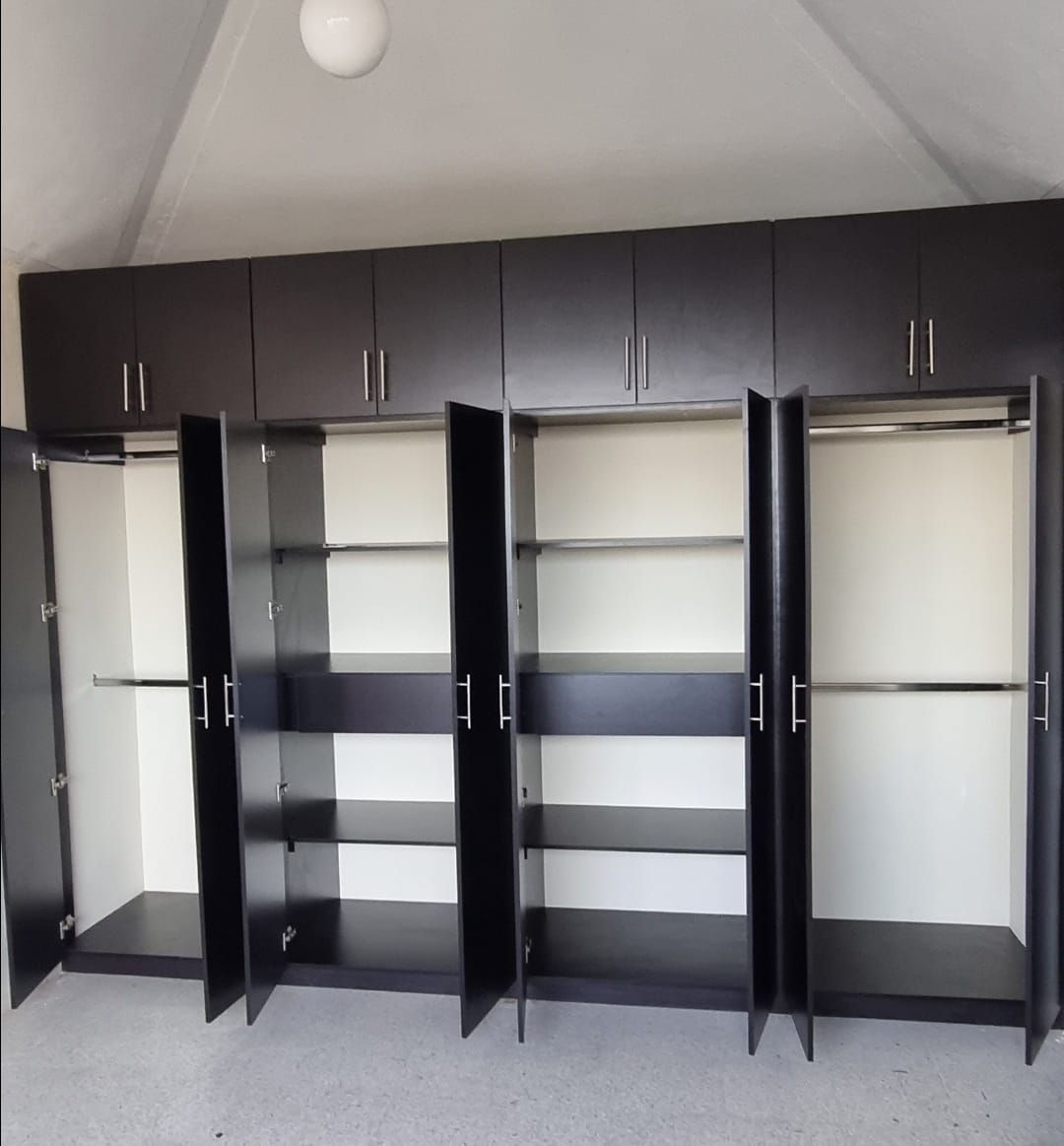 Armario oscuro abierto con múltiples estantes y secciones para colgar ropa en una habitación luminosa.