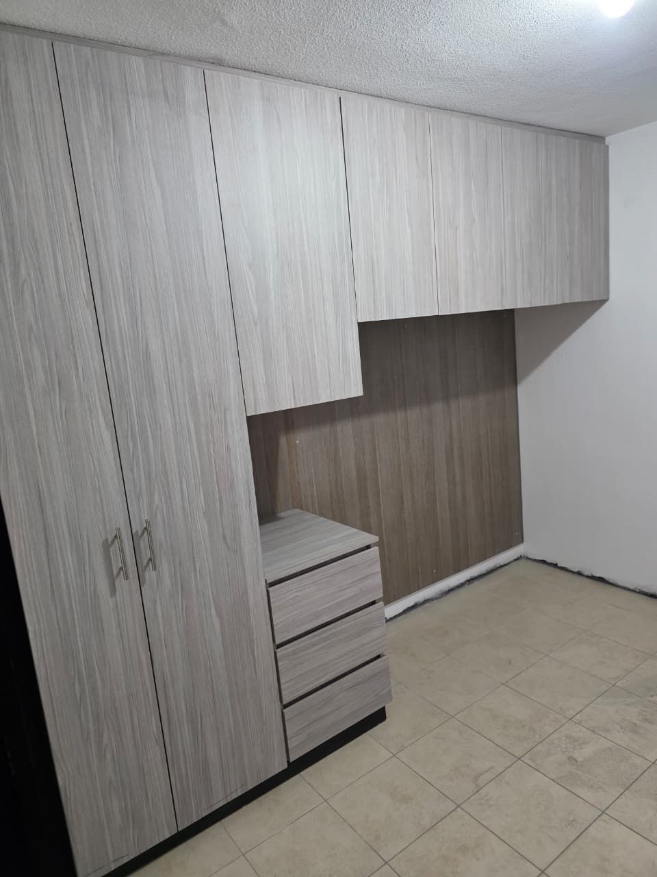 Armarios empotrados de madera blanca con cajones en una habitación alicatada.