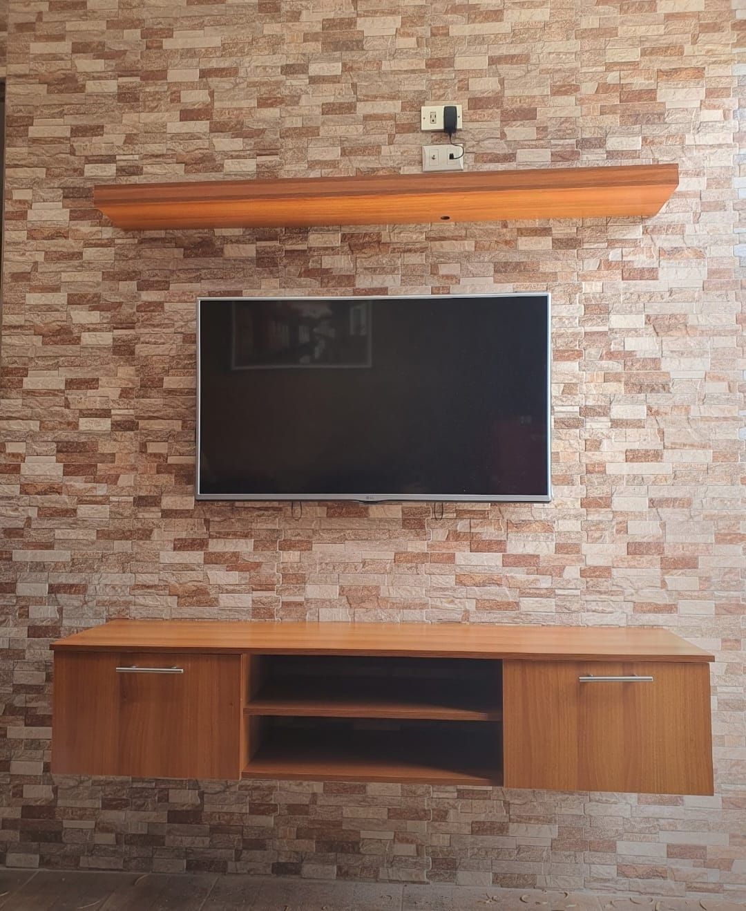 Televisor montado en la pared sobre una pared decorativa con diseño de piedra, estantes de madera y un mueble
