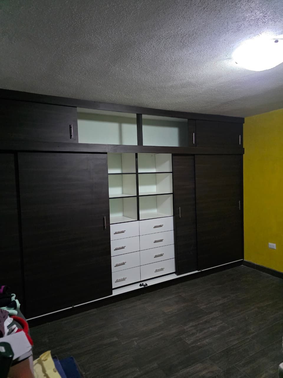 Habitación vacía con armario oscuro, cajones blancos y una luz brillante en el techo.