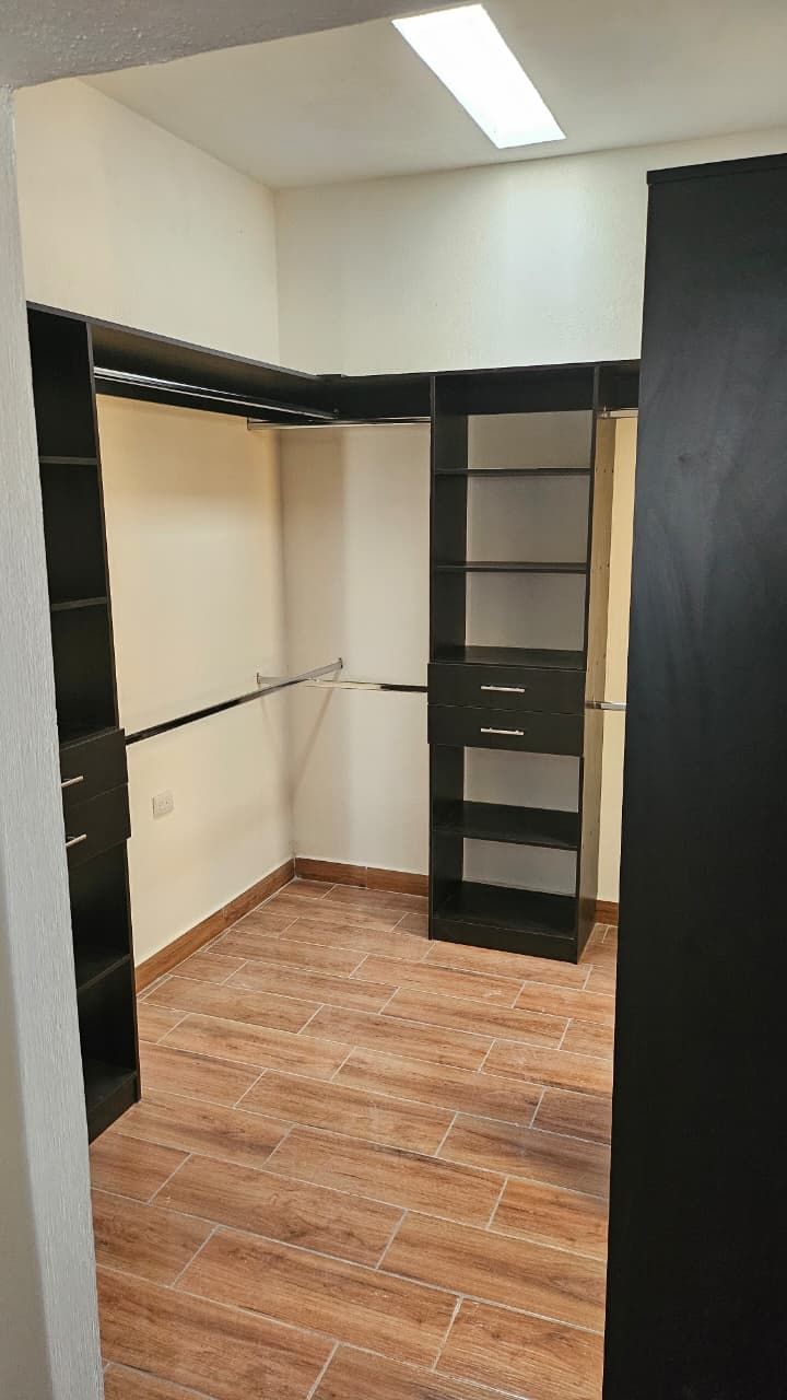 Vestidor vacío con estantes y barras para colgar ropa de color negro, suelo con aspecto de madera y luz de techo.