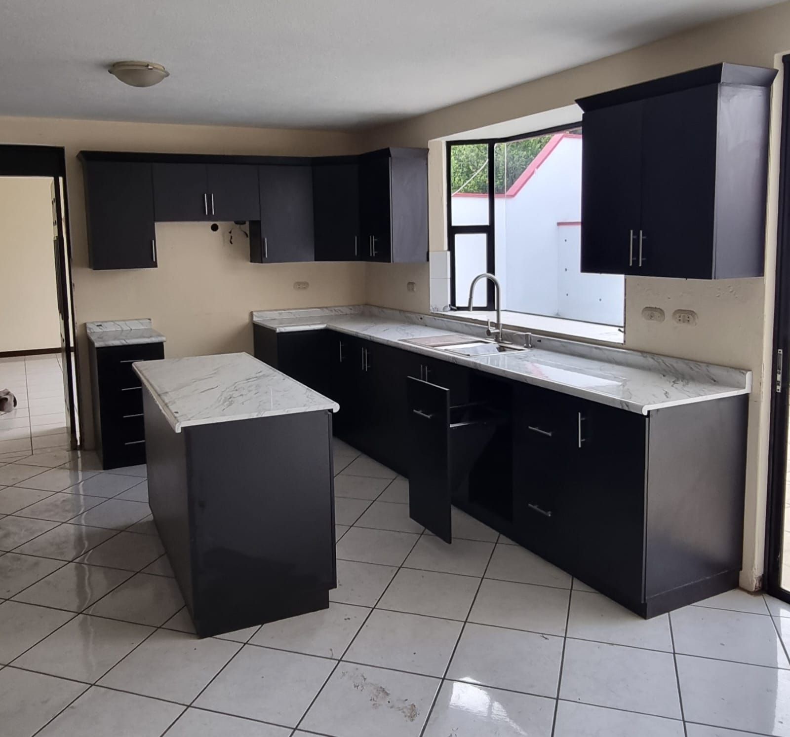 Cocina moderna con armarios oscuros, isla, suelo de baldosas y una ventana sobre el fregadero.