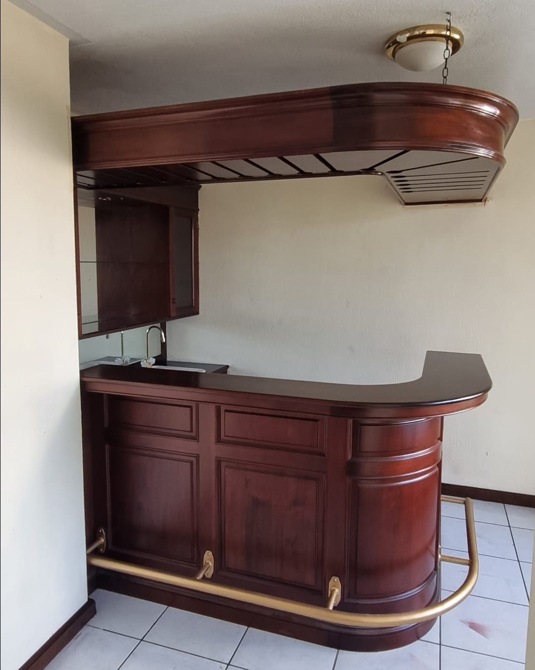 Barra de bar esquinera de madera con gabinetes oscuros, encimera negra y estante superior.
