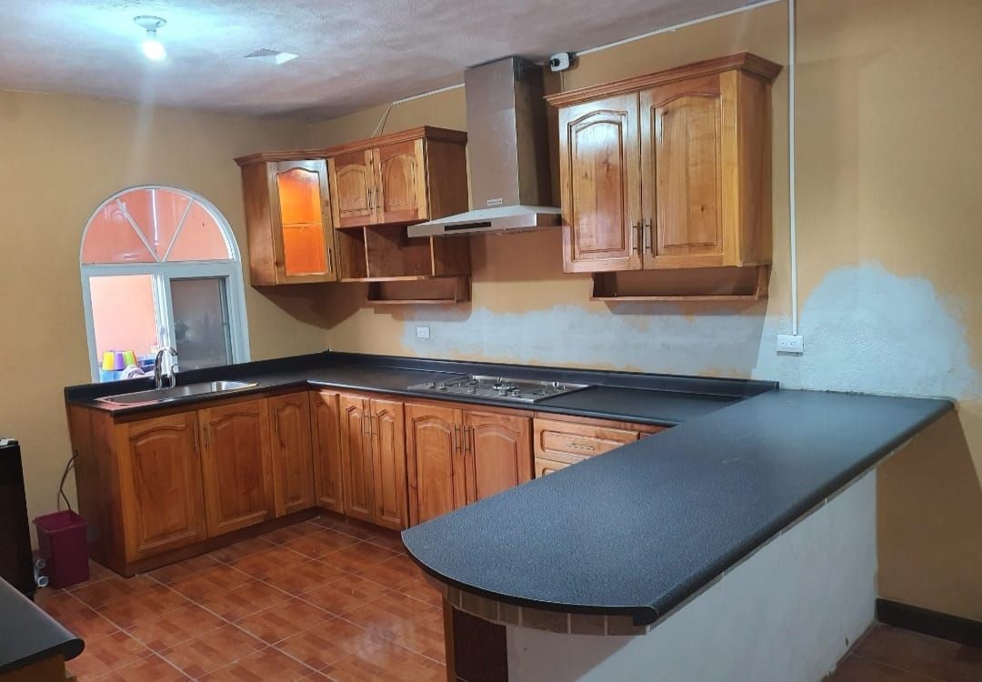 Cocina de madera con encimeras oscuras, armarios superiores y una ventana arqueada a la izquierda.