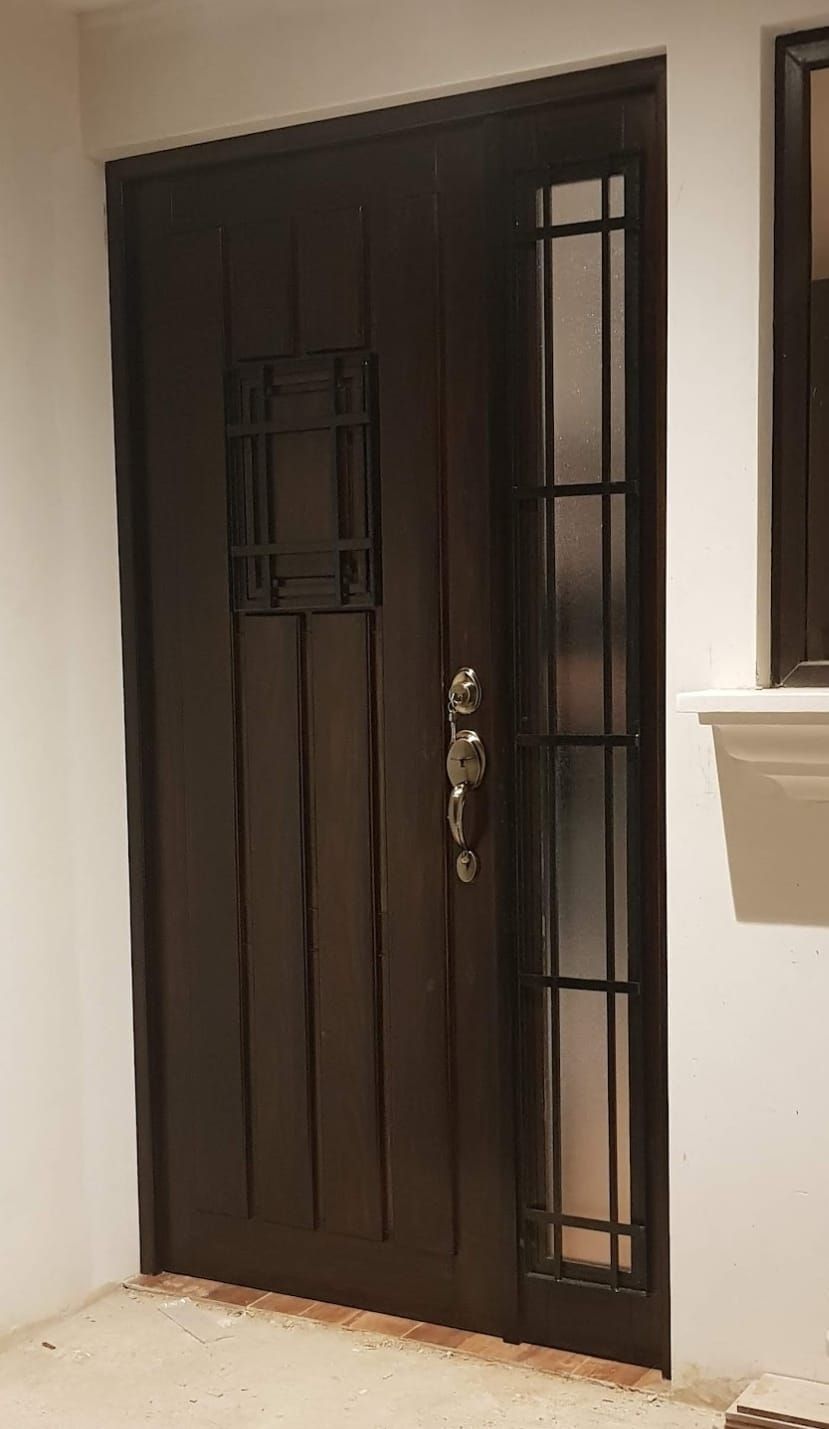 Puerta principal de metal negro con paneles de vidrio y manija plateada en una pared blanca.