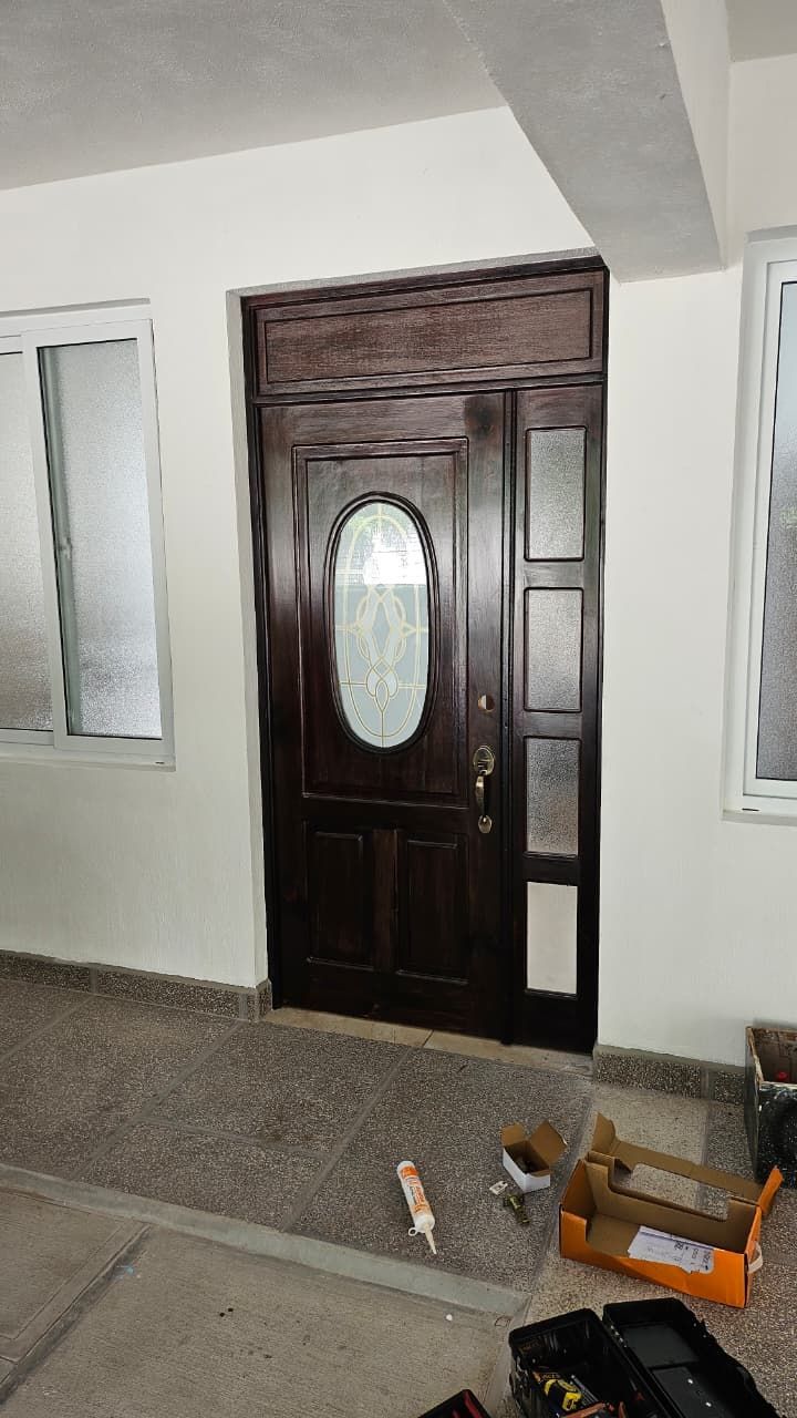 Puerta principal de madera oscura con panel de vidrio