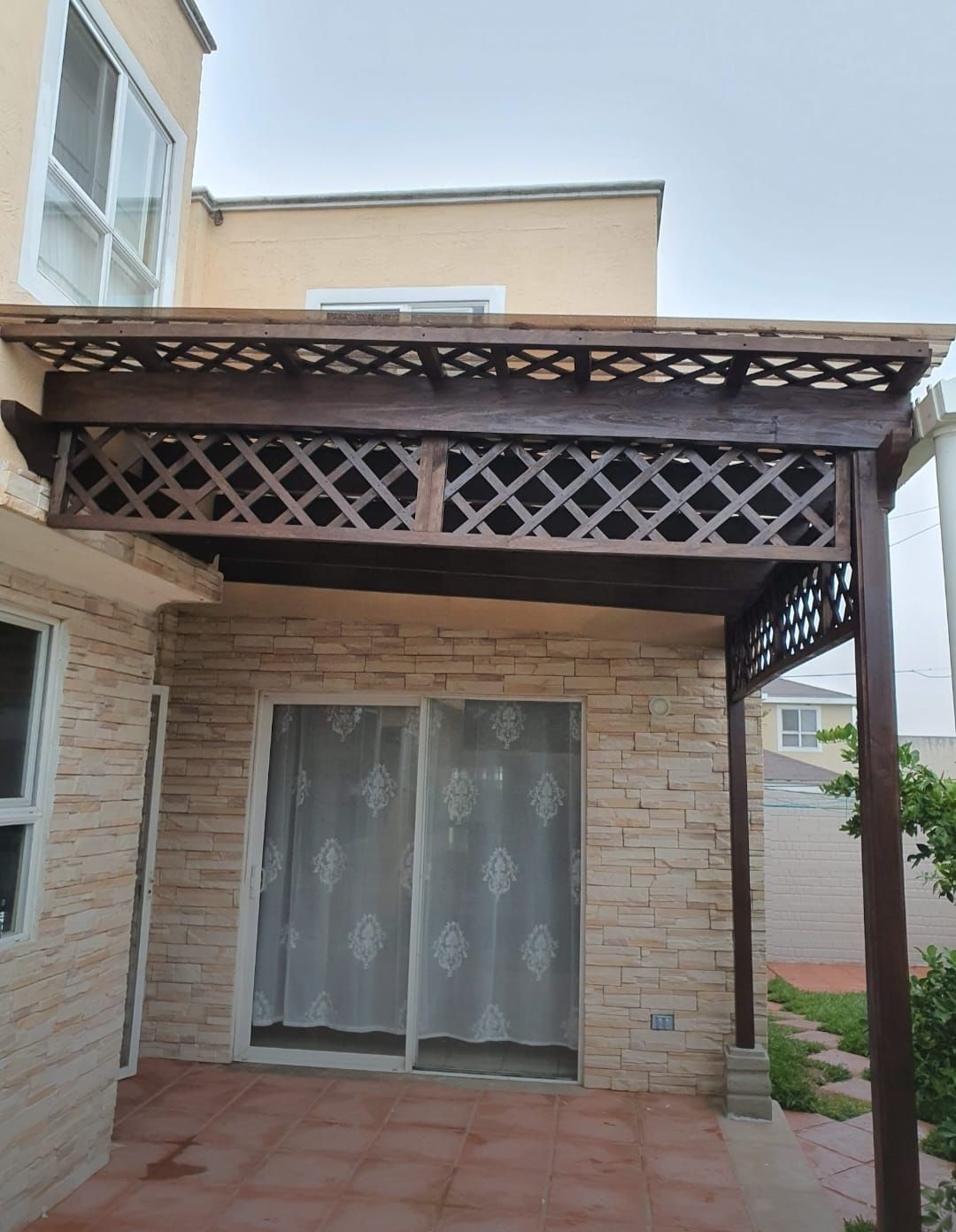 Patio cubierto con muro de ladrillo, celosía de madera y puerta corrediza de vidrio.
