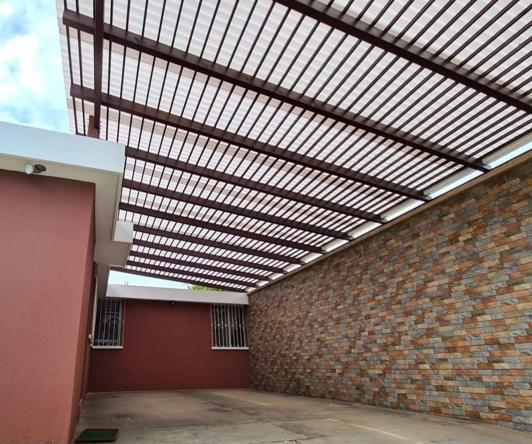 Patio cubierto con techo de chapa ondulada, pared de ladrillo, edificio rojo y suelo de hormigón.