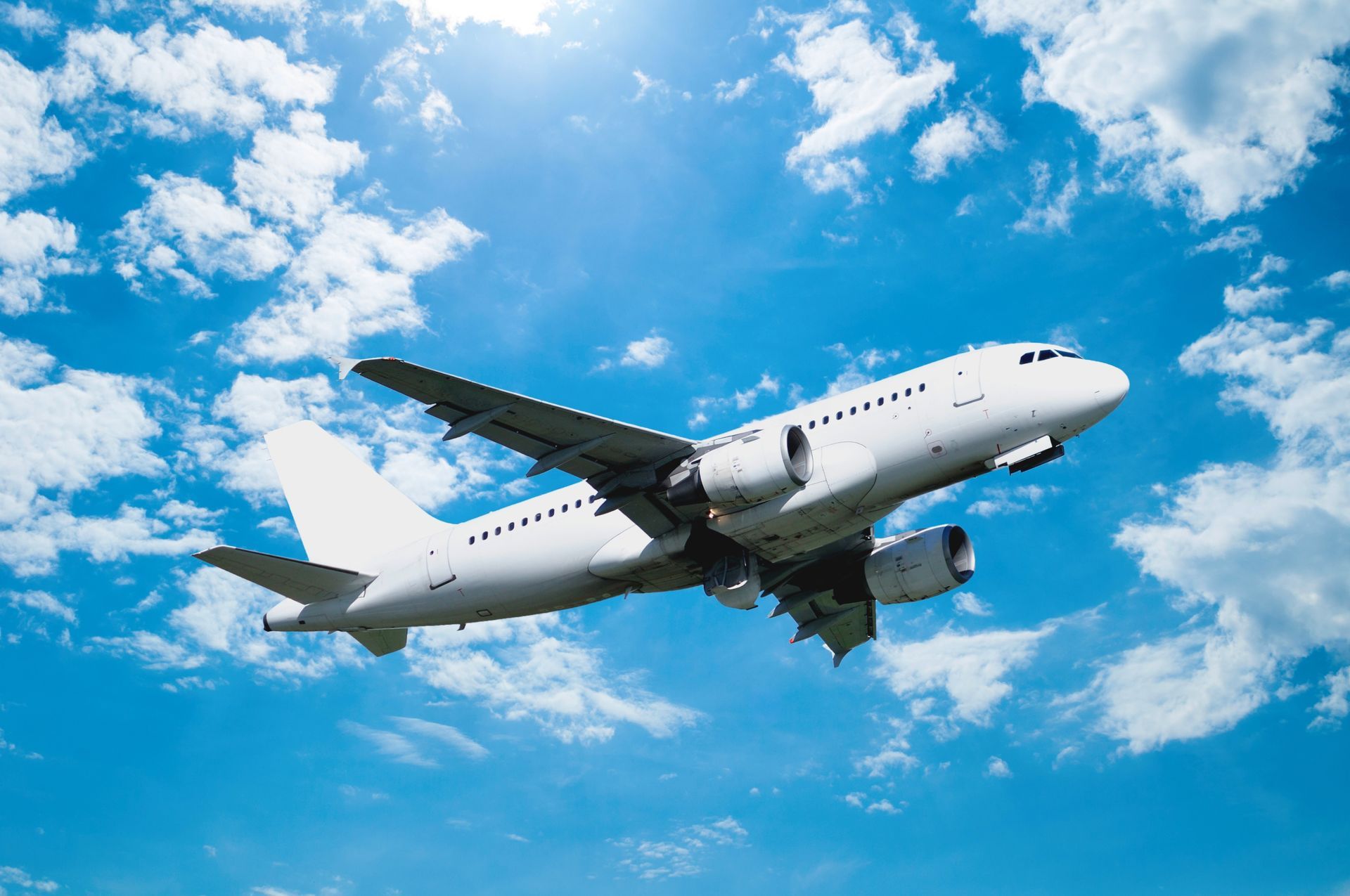 White commercial airplane flying against a bright blue sky with scattered clouds