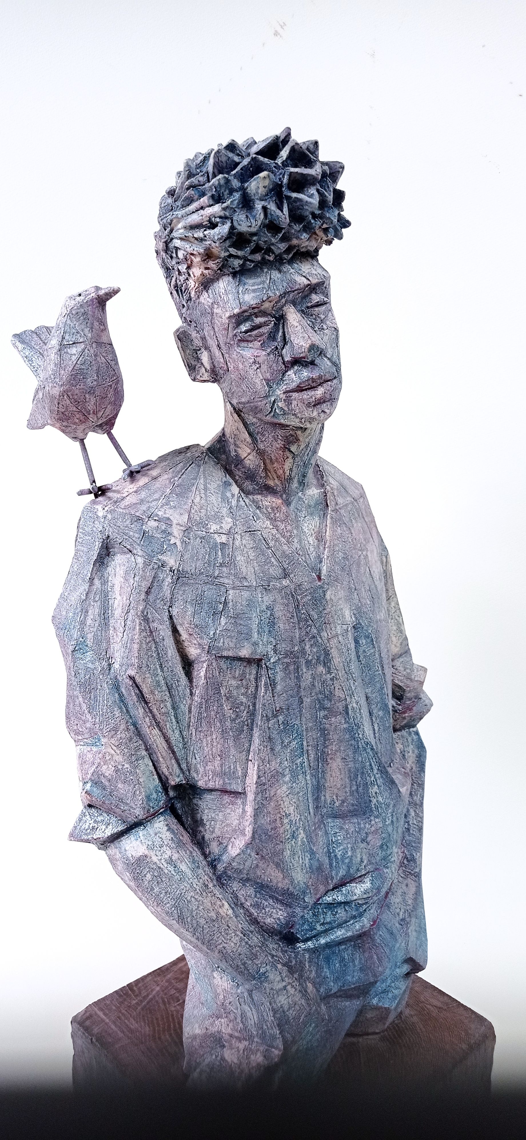 Sculpture of a person with bird on shoulder. Gray tones, geometric form.