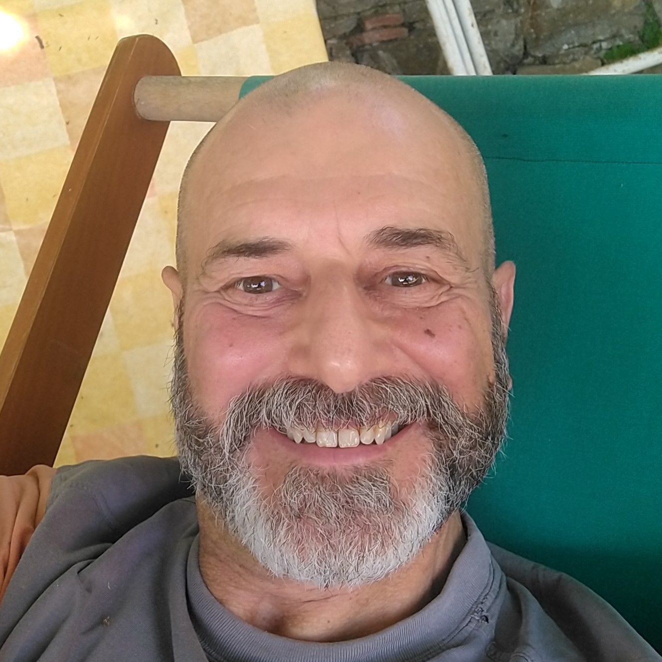 artist Fabrizio Tiribilli with gray beard smiles, sitting in green chair outdoors.