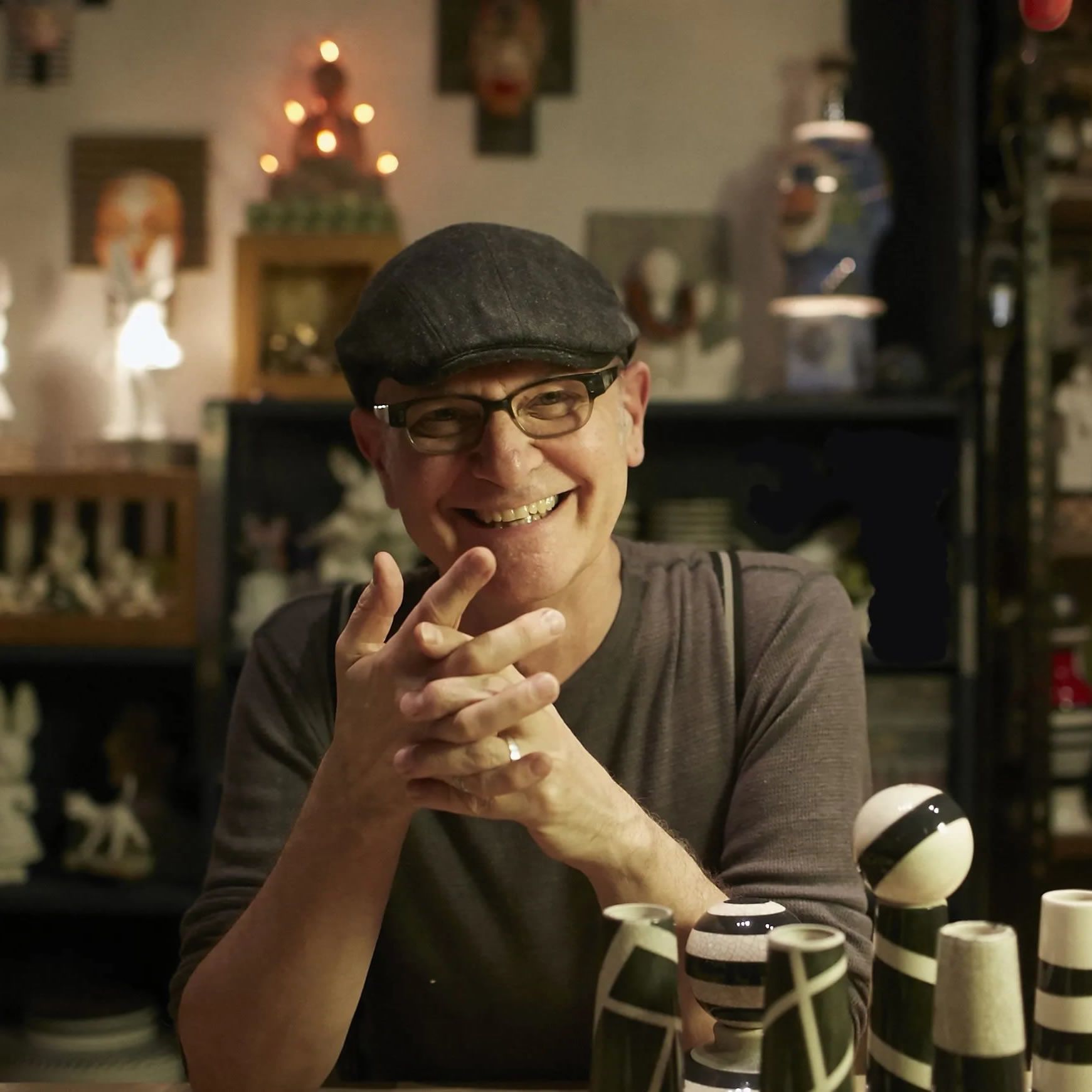 Man in glasses and cap smiles in a shop with ceramic art.