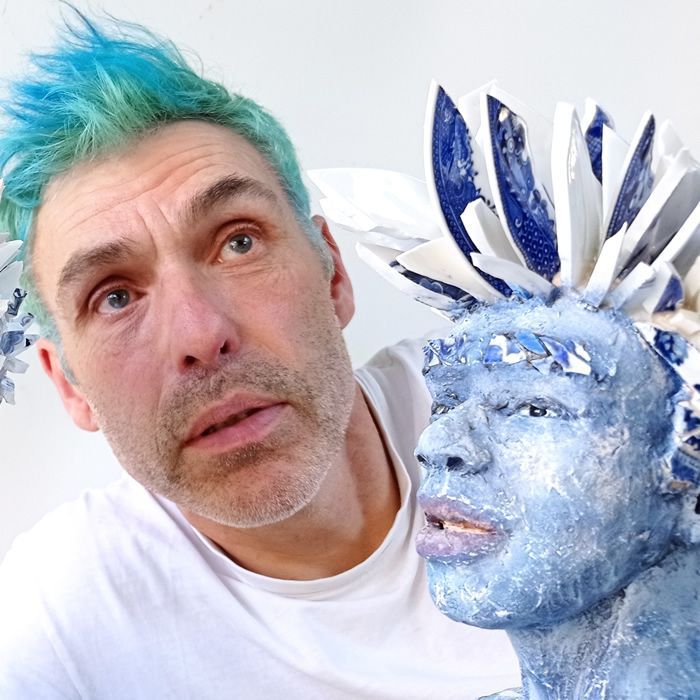 Artist peter garrard with blue hair, looking up, poses with blue sculpture.