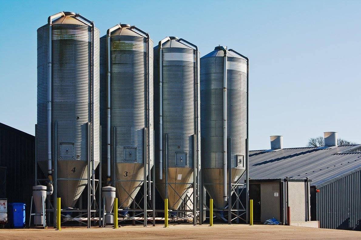 Four metal silos against a blue sky; next to a low building.