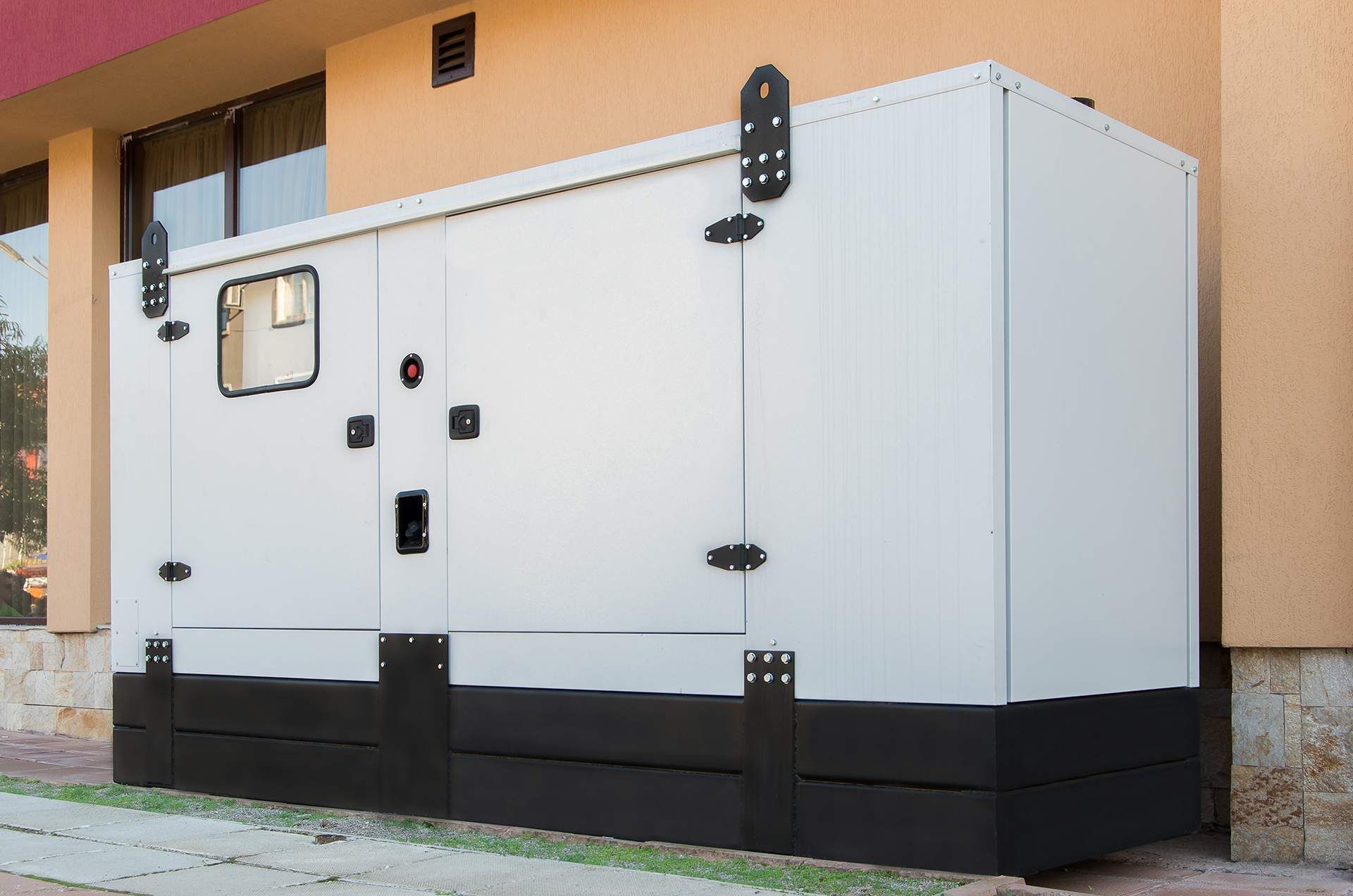 White outdoor generator enclosure with black base beside a building