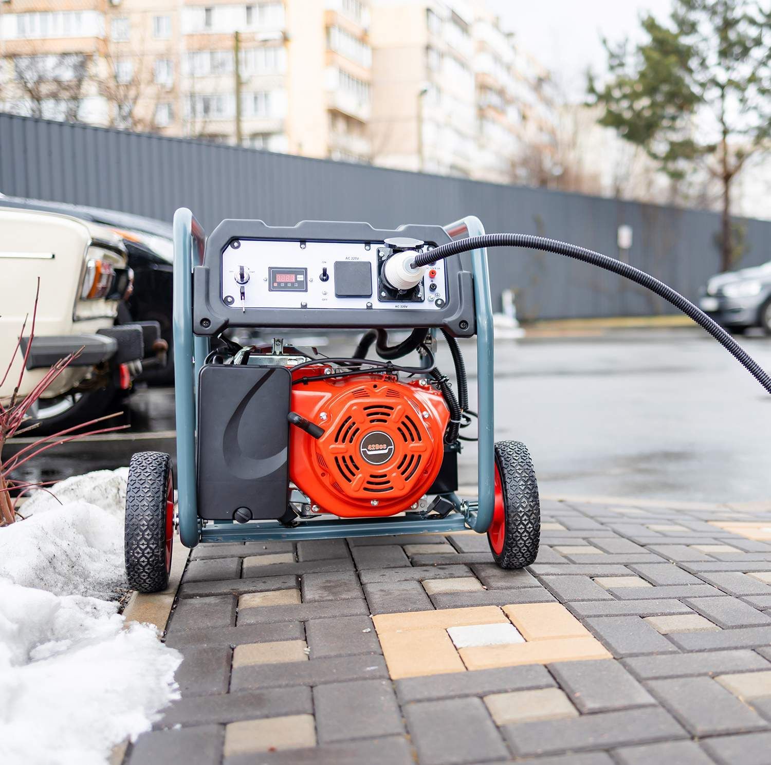 Portable orange generator outside on a brick path, connected to an electrical cord.