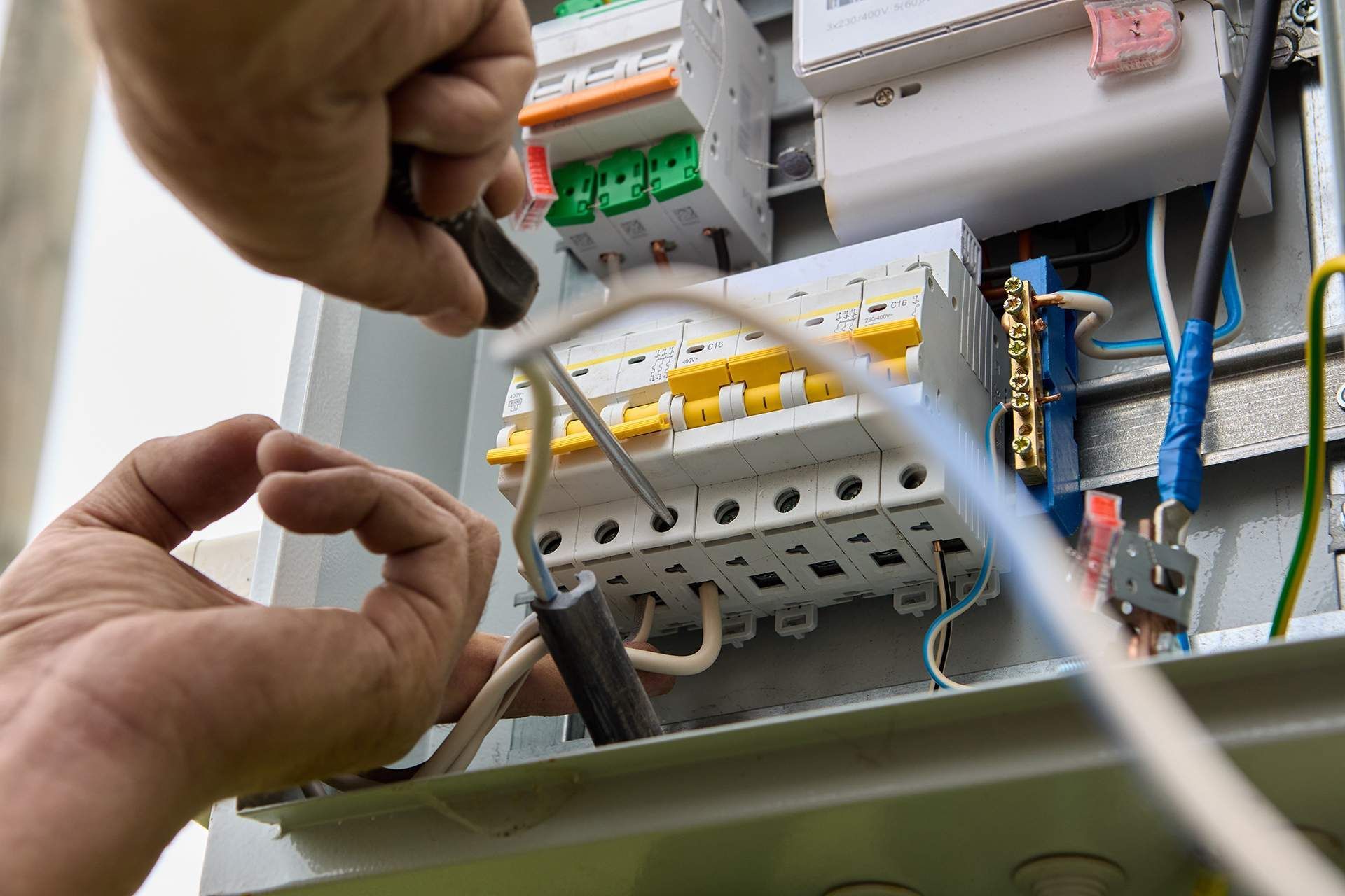 Electrician working on a circuit breaker box, using a screwdriver; close-up view.