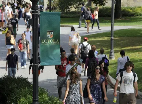 People walking on a Loyola University campus path; banner with school logo in the foreground.