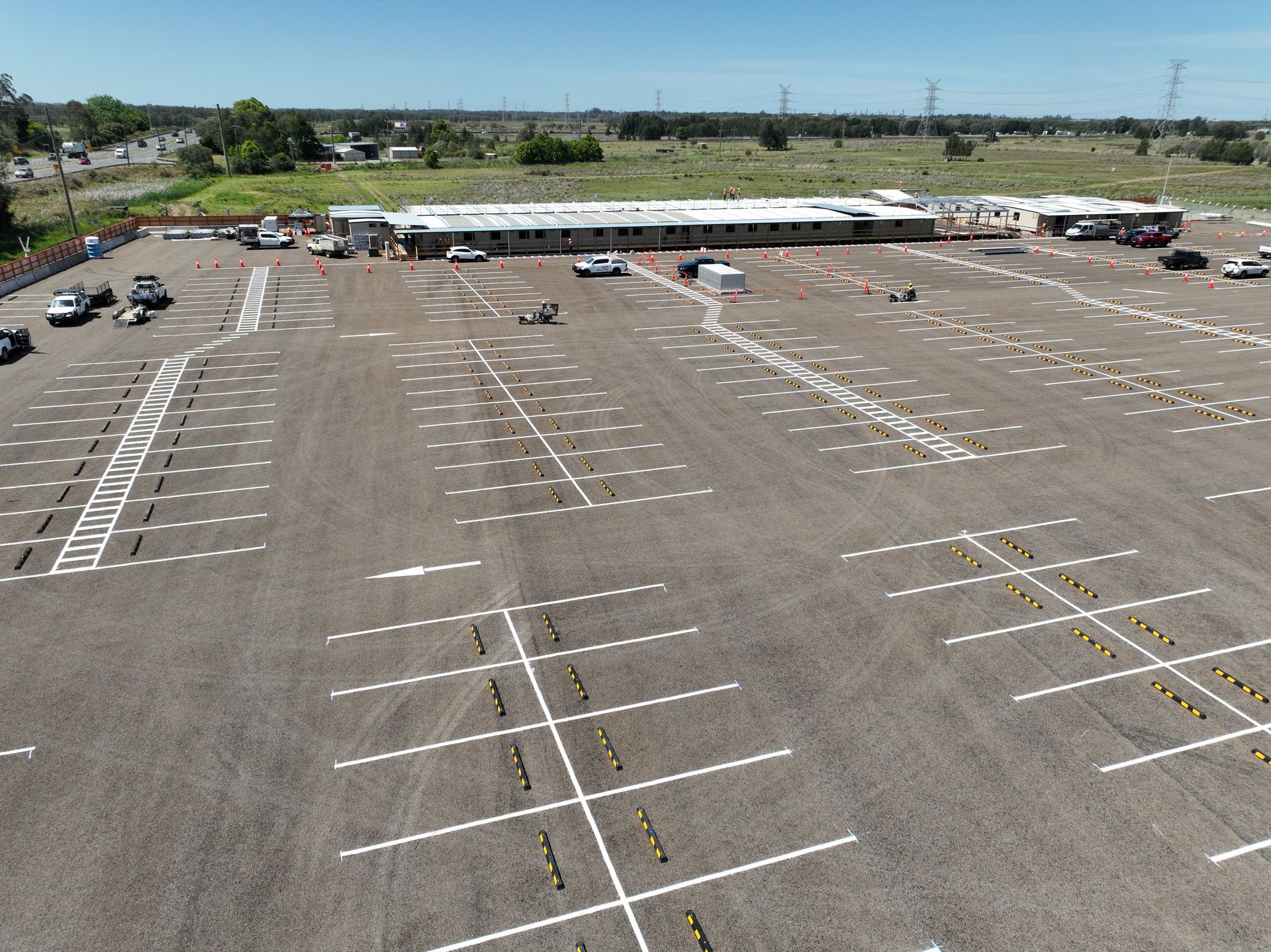 Empty outdoor parking lot with painted white lines and a few cars along the far edge. Empty outdoor parking lot with painted white lines and a few cars along the far edge.